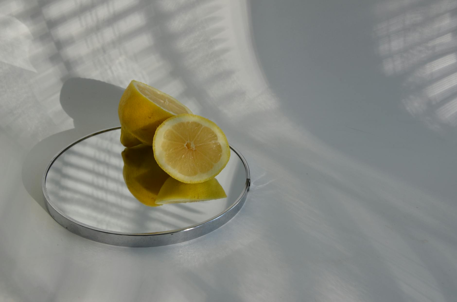A hand with white nails holding a lemon on a soft pink background, surrounded by three additional lemons.