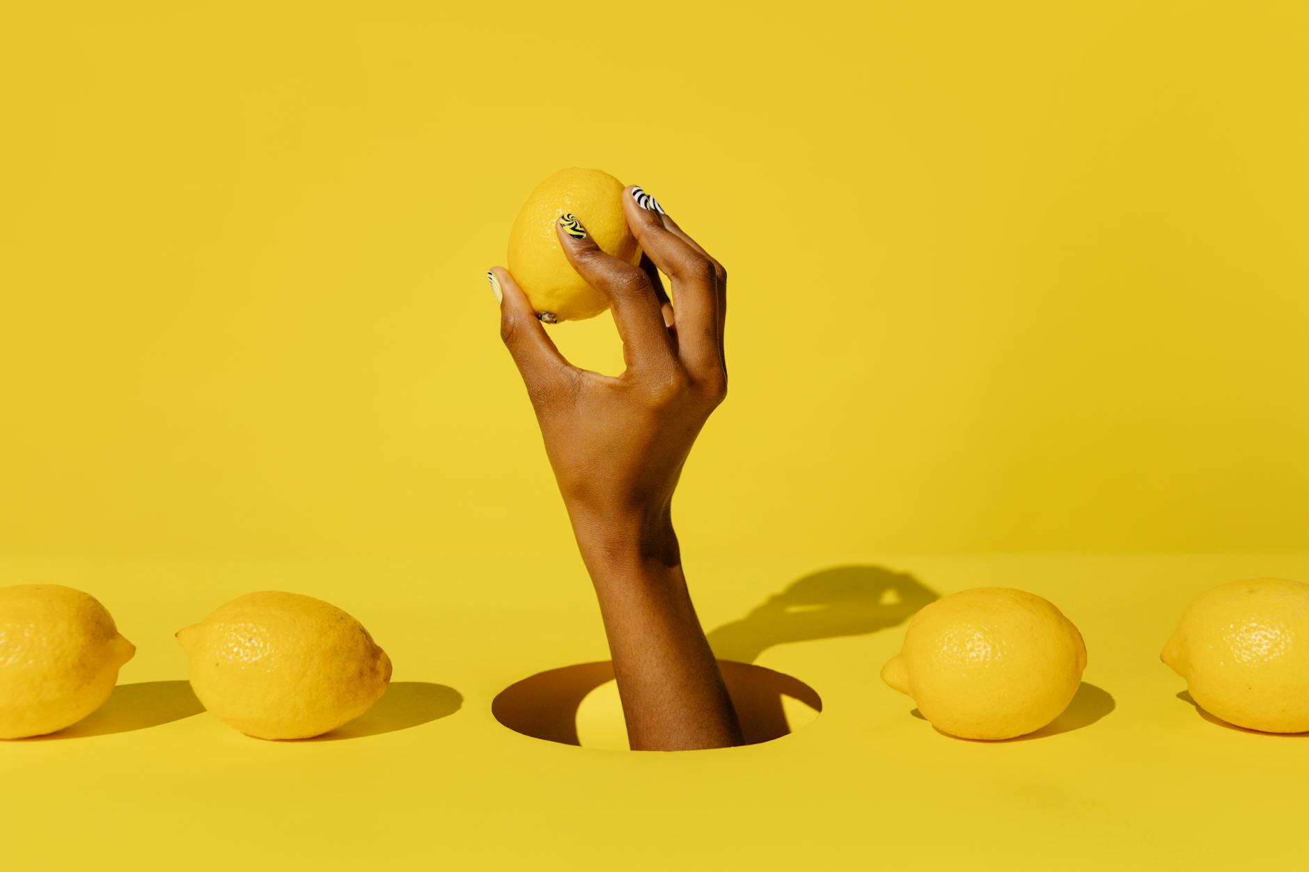 A hand holding a fresh lemon against a bright yellow background, symbolizing presence and sensation.