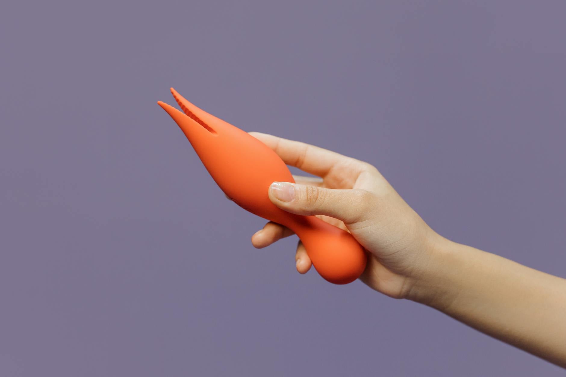A hand holding a lemon vibrator against a minimalistic purple backdrop, showcasing intimate partner play.