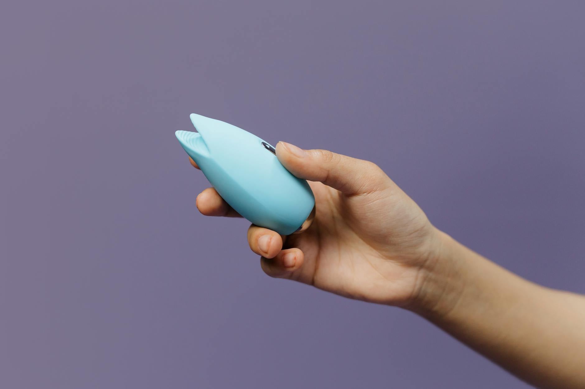 A person holding a blue silicone vibrator against a solid purple background