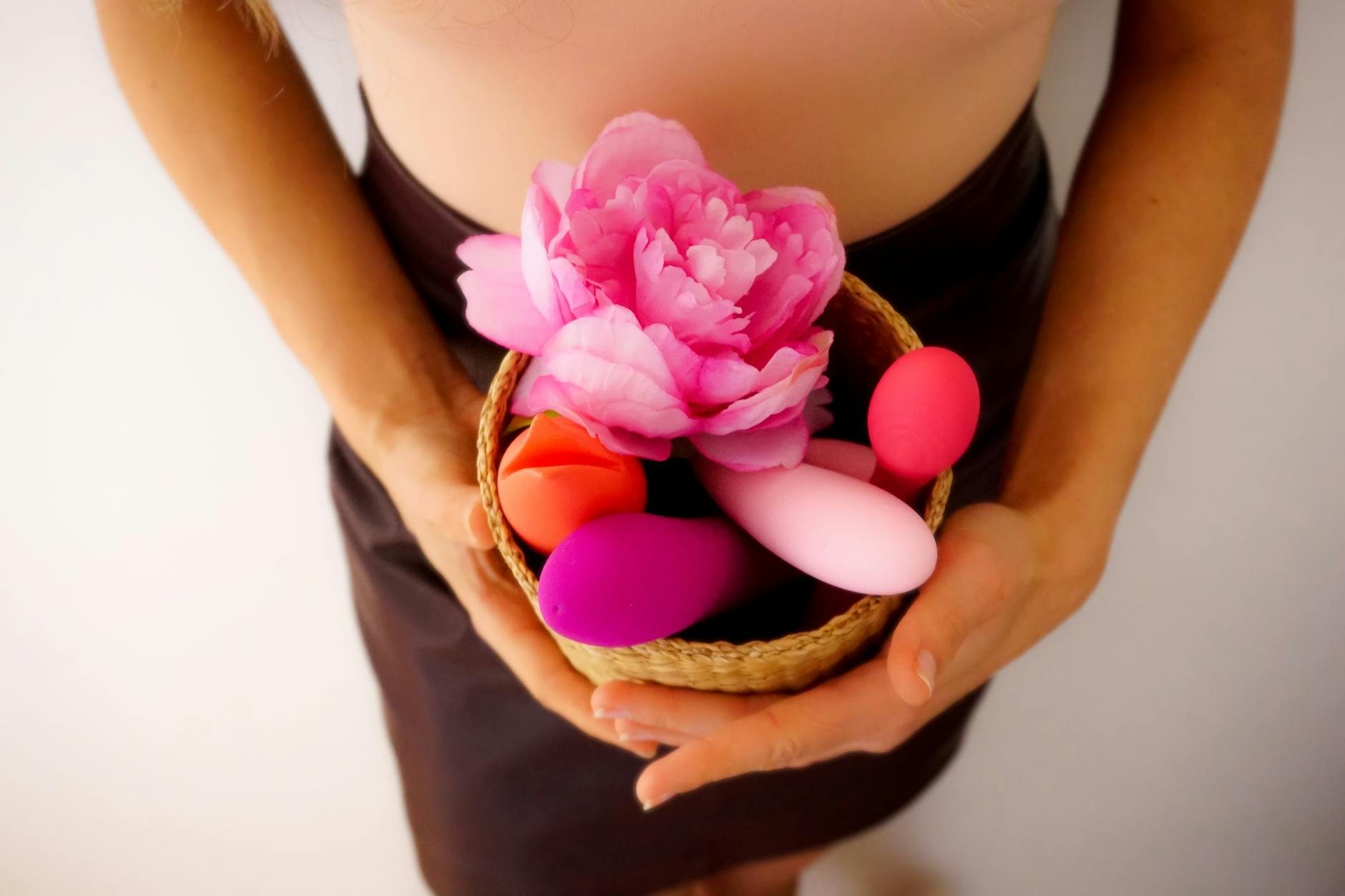 A basket of colorful vibrators and a pink flower representing pleasure and self-care in midlife